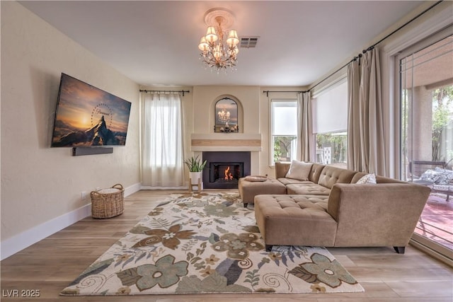 living area featuring visible vents, baseboards, a glass covered fireplace, wood finished floors, and an inviting chandelier