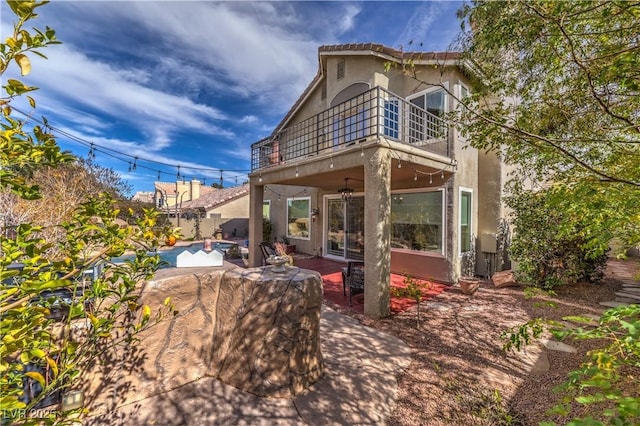 back of house featuring a balcony, a fenced in pool, a patio, and stucco siding