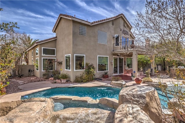 rear view of house featuring a pool with connected hot tub, a patio, a balcony, and stucco siding