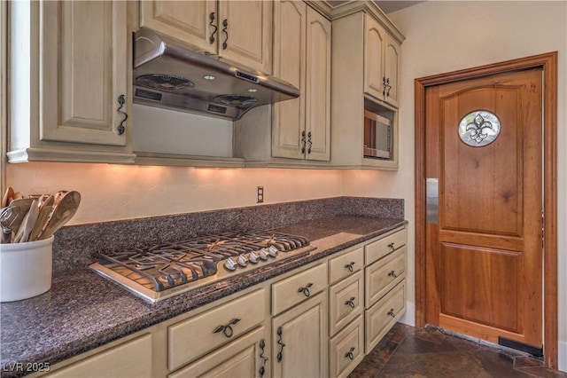 kitchen featuring stainless steel gas cooktop, cream cabinets, dark stone countertops, and under cabinet range hood