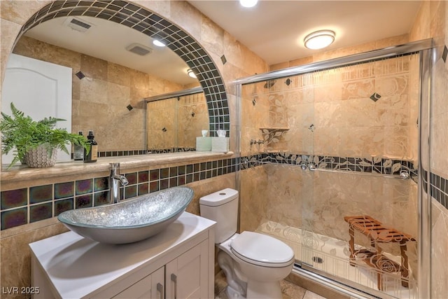 bathroom with tile walls, visible vents, toilet, a stall shower, and vanity