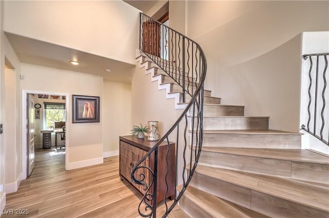 stairway with wood finished floors, a towering ceiling, and baseboards