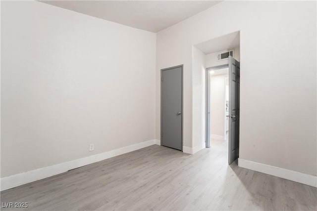 empty room with light wood-type flooring, visible vents, and baseboards