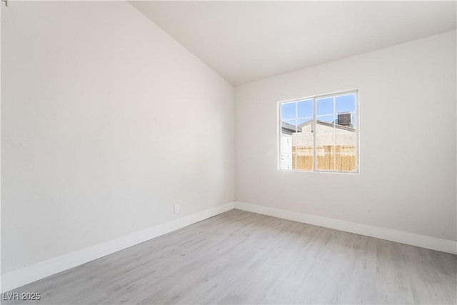 spare room featuring light wood finished floors, baseboards, and vaulted ceiling