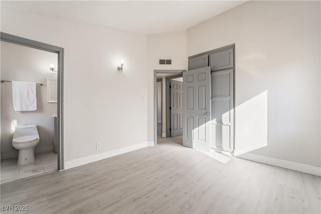 unfurnished bedroom featuring visible vents, ensuite bath, baseboards, and wood finished floors