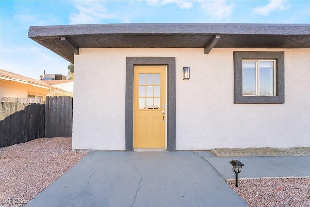 entrance to property featuring fence, a patio, and stucco siding