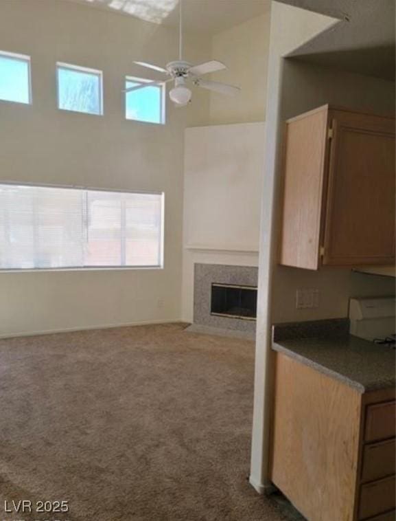 unfurnished living room featuring dark colored carpet, a fireplace, a towering ceiling, and a ceiling fan