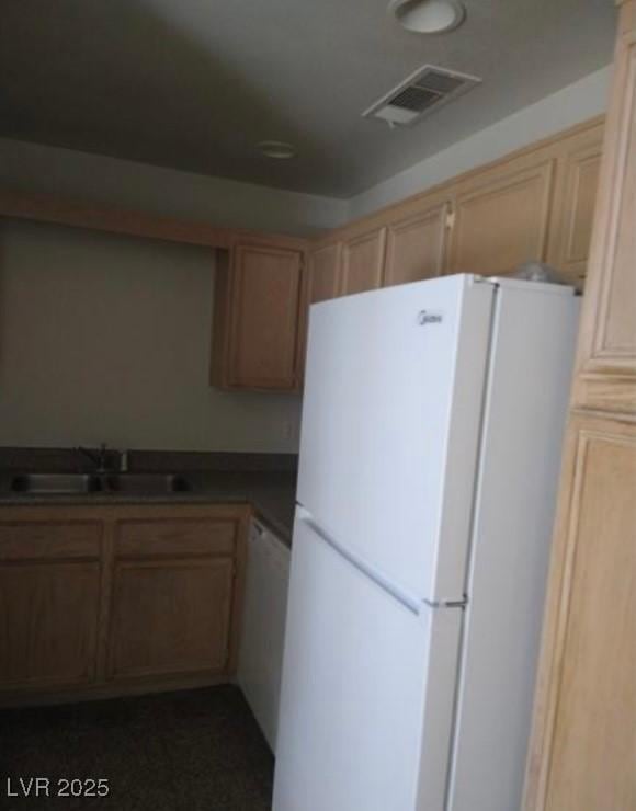 kitchen with dark countertops, white appliances, visible vents, and a sink