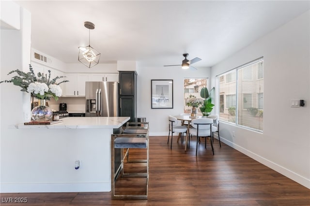 kitchen featuring stainless steel fridge, visible vents, dark wood finished floors, baseboards, and a peninsula