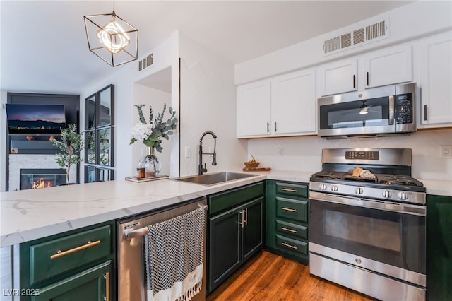 kitchen with white cabinetry, visible vents, stainless steel appliances, and a glass covered fireplace