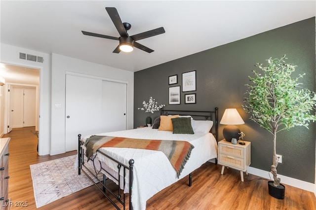 bedroom featuring ceiling fan, wood finished floors, visible vents, baseboards, and a closet