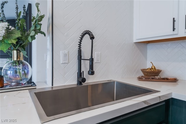 interior details with light stone counters, backsplash, a sink, and white cabinetry