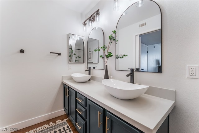 bathroom featuring wood finished floors, a sink, baseboards, and double vanity