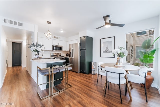 kitchen with visible vents, appliances with stainless steel finishes, wood finished floors, a peninsula, and light countertops