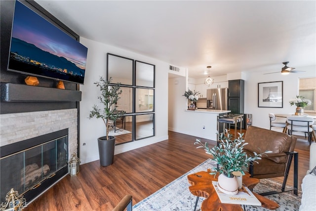 living area featuring ceiling fan, visible vents, wood finished floors, and a stone fireplace