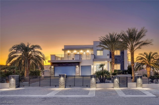 contemporary house with a fenced front yard, a gate, a balcony, and stucco siding