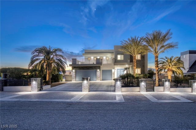 contemporary home with a balcony, a fenced front yard, driveway, and a garage