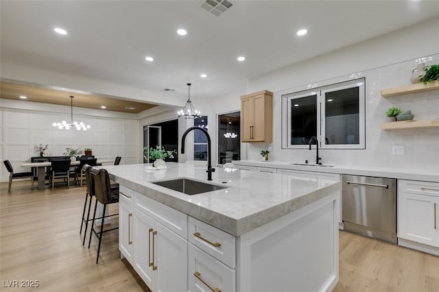 kitchen featuring dishwasher, an island with sink, a sink, and visible vents