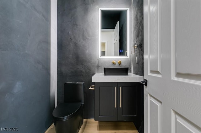 half bathroom with vanity, toilet, and wood finished floors