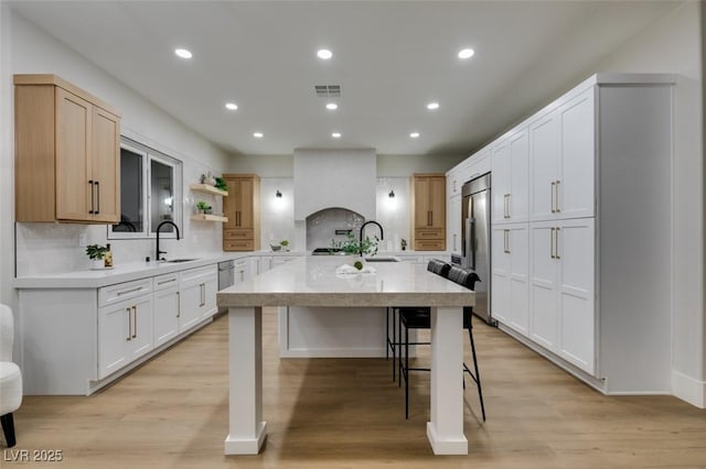 kitchen with a center island with sink, visible vents, built in refrigerator, light countertops, and a sink