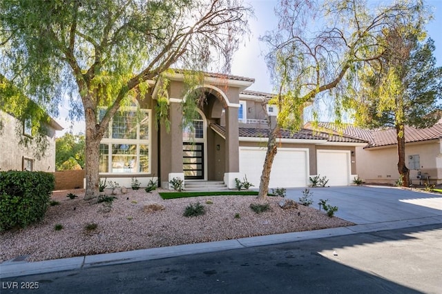 mediterranean / spanish house featuring a garage, driveway, a tiled roof, and stucco siding