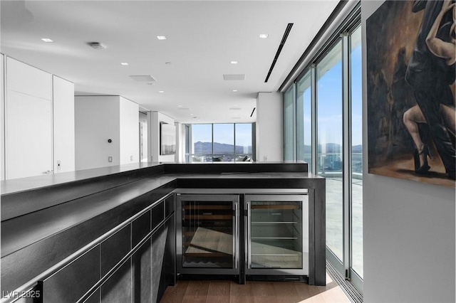 bar featuring dark wood-type flooring, wine cooler, visible vents, and expansive windows