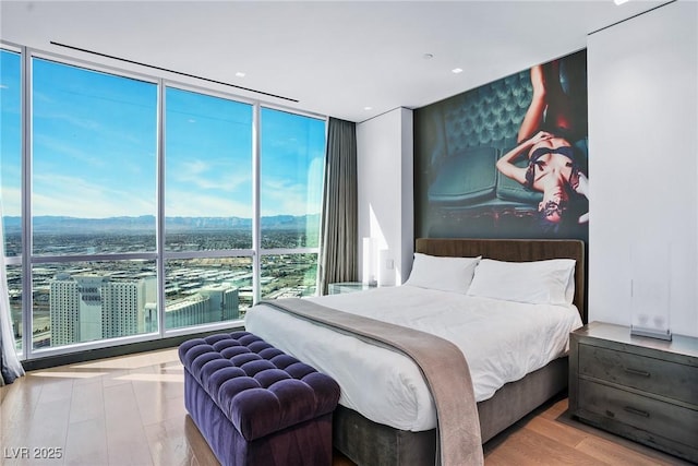 bedroom with a view of city, floor to ceiling windows, and wood finished floors