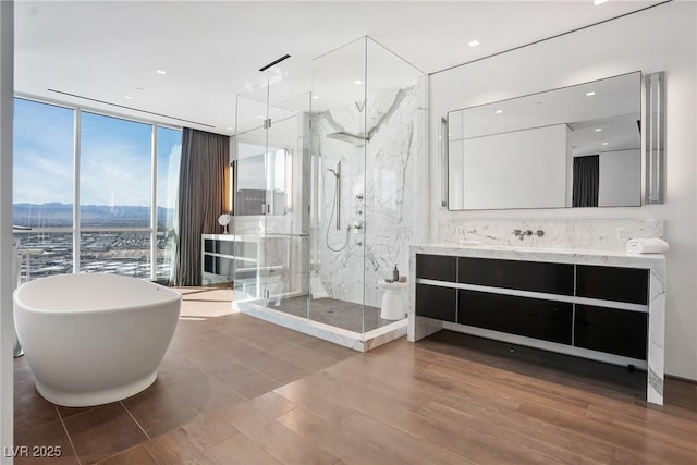 full bathroom featuring wood finished floors, vanity, a soaking tub, a marble finish shower, and a wall of windows