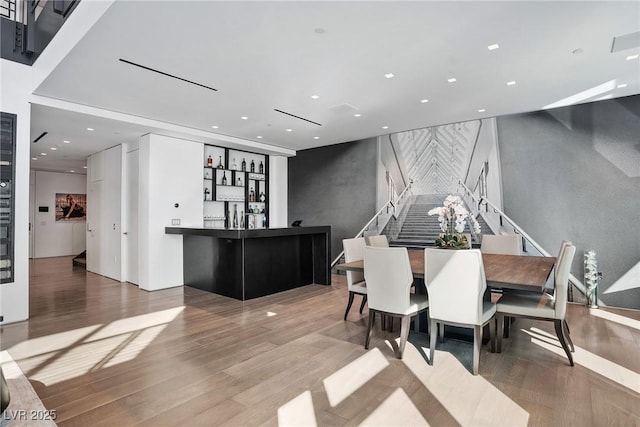 dining space featuring stairs, an accent wall, indoor wet bar, and wood finished floors