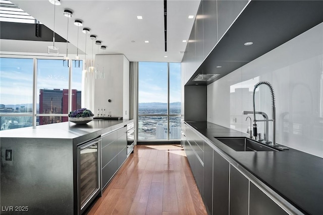 kitchen with beverage cooler, a wall of windows, modern cabinets, and a sink