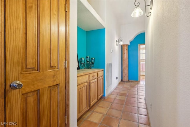 hallway with light tile patterned floors, baseboards, visible vents, and arched walkways