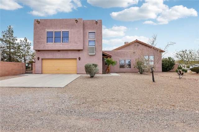 pueblo-style home with an attached garage, fence, concrete driveway, and stucco siding