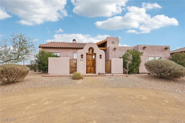 view of front of home featuring a fenced front yard, a tile roof, a gate, stucco siding, and a chimney