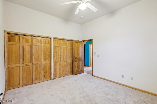 unfurnished bedroom with a ceiling fan, light colored carpet, baseboards, and two closets