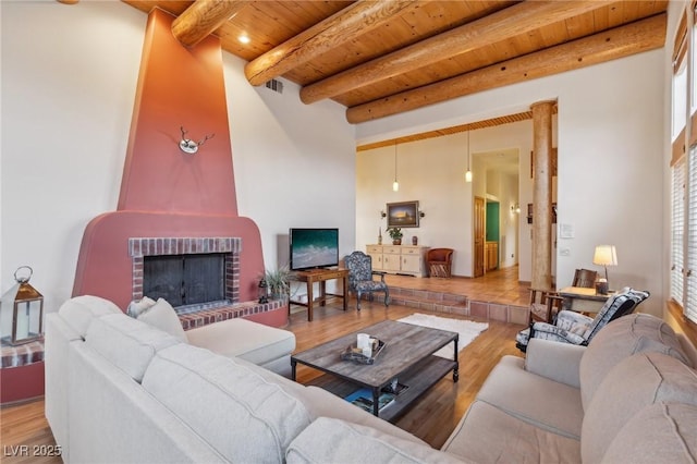 living room with wood ceiling, a brick fireplace, beamed ceiling, and wood finished floors