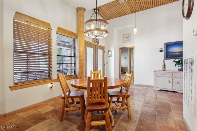 dining area featuring an inviting chandelier, stone tile floors, a high ceiling, and french doors