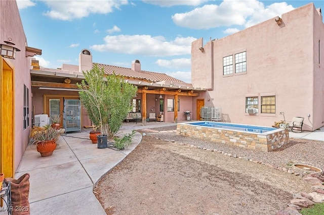 back of property featuring a hot tub, a chimney, cooling unit, a patio area, and stucco siding