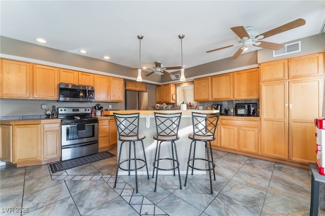 kitchen with visible vents, a ceiling fan, a kitchen breakfast bar, a center island, and stainless steel appliances