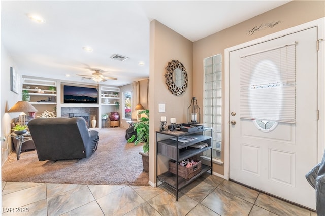 tiled entryway with carpet floors, ceiling fan, visible vents, and a tiled fireplace