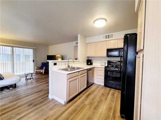 kitchen with light wood finished floors, visible vents, a sink, a peninsula, and black appliances