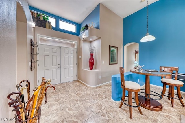 entryway featuring arched walkways, high vaulted ceiling, and baseboards