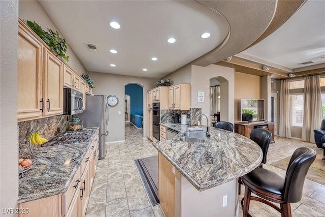 kitchen with arched walkways, stainless steel appliances, a sink, and light brown cabinetry