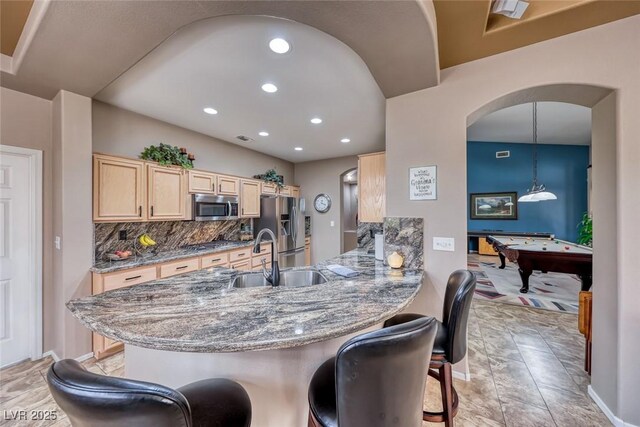 kitchen featuring light brown cabinets, stainless steel appliances, a sink, a kitchen breakfast bar, and tasteful backsplash