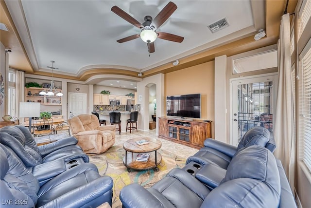 living area featuring visible vents, arched walkways, a tray ceiling, and ceiling fan with notable chandelier