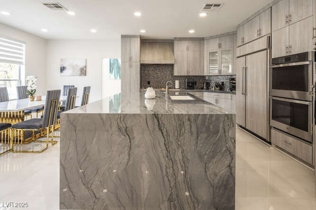 kitchen featuring visible vents, modern cabinets, custom range hood, built in refrigerator, and stainless steel double oven