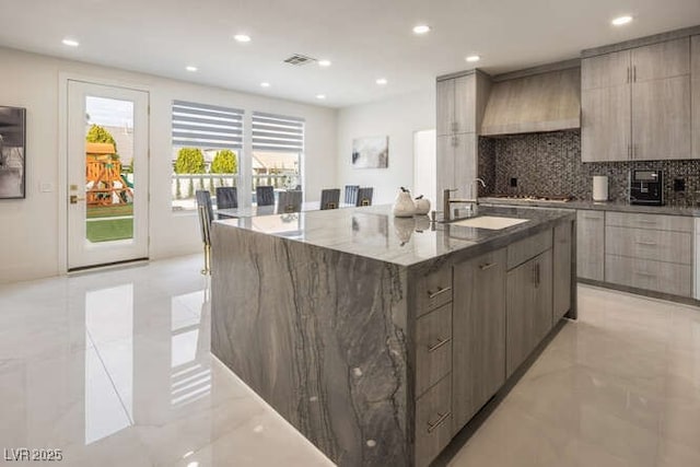 kitchen with a sink, a large island, custom exhaust hood, dark stone counters, and modern cabinets