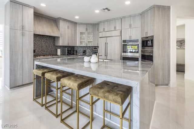 kitchen featuring stainless steel appliances, visible vents, custom exhaust hood, light stone countertops, and tasteful backsplash