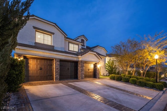 view of front facade with a garage, driveway, stone siding, and stucco siding