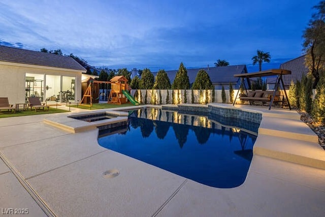 pool at dusk with a pool with connected hot tub, fence, a playground, and a patio