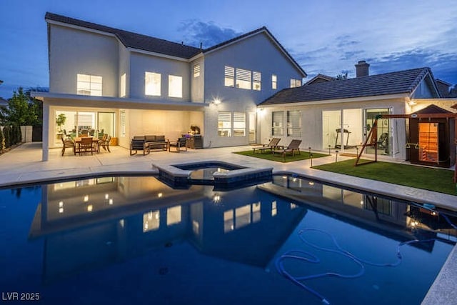 back of property at dusk featuring a patio area, a pool with connected hot tub, an outdoor living space, and stucco siding